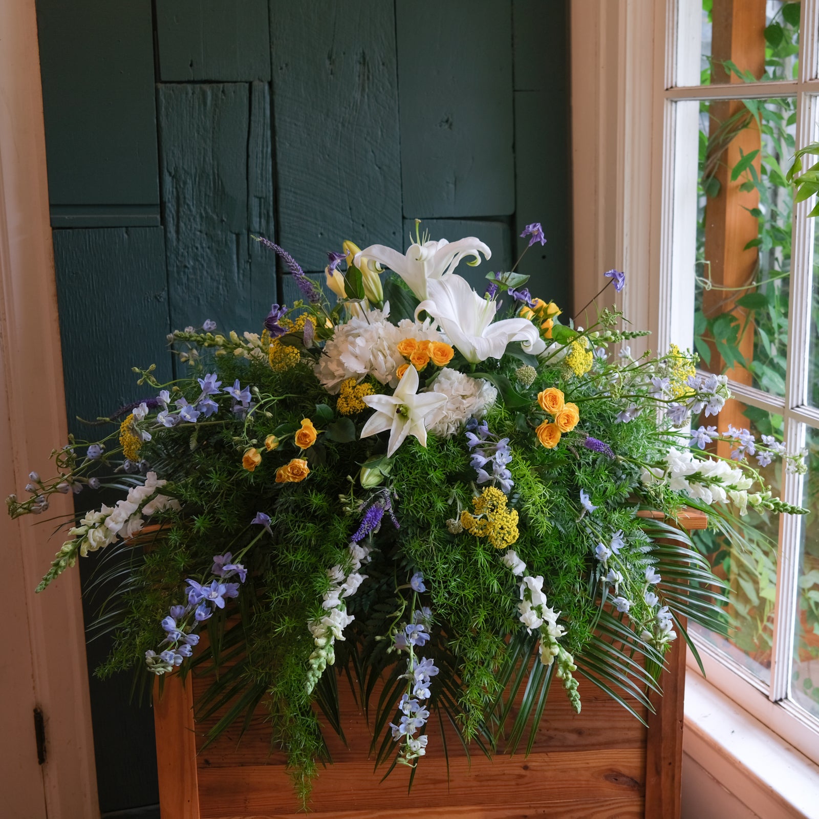 A floral spray featuring white lilies, hydrangea, blue flowers and yellow accents.