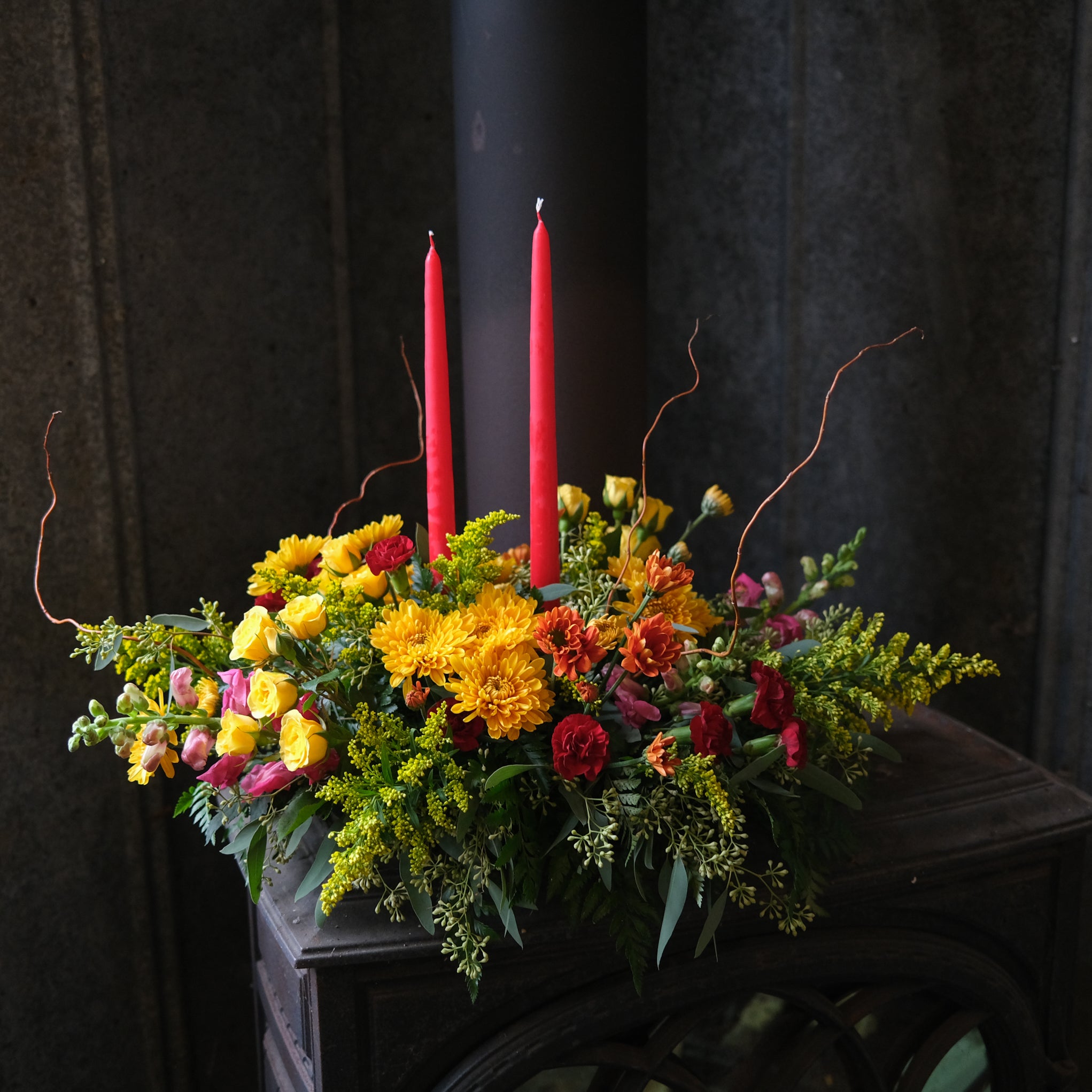 yellow spray rose, mums, salidago, red carnations, pink snapdragons, and eucalyptus with red taper candles