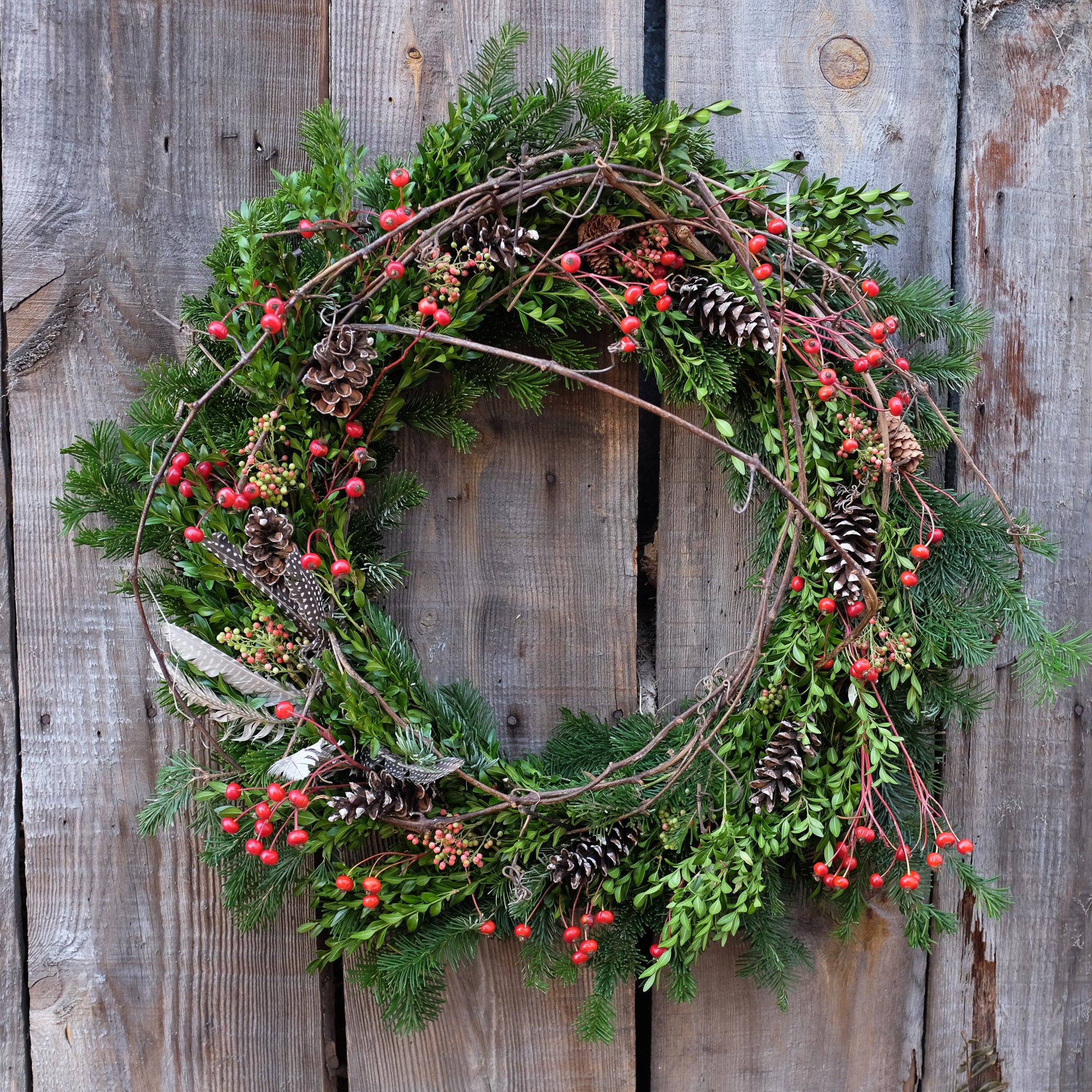 mixed evergreen wreath with pinecones, winter berries, feathers, and winding stick accents by Michler's