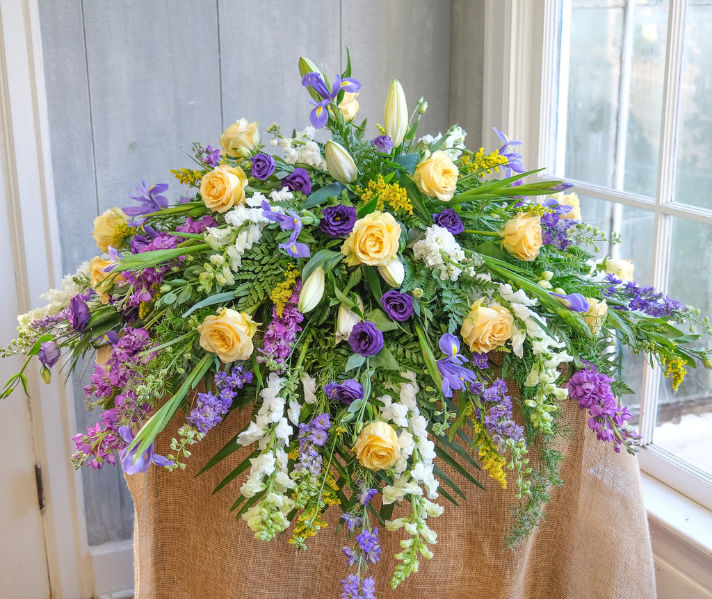floral casket spray with roses, ranunculus, lilies, and stock by Michler's