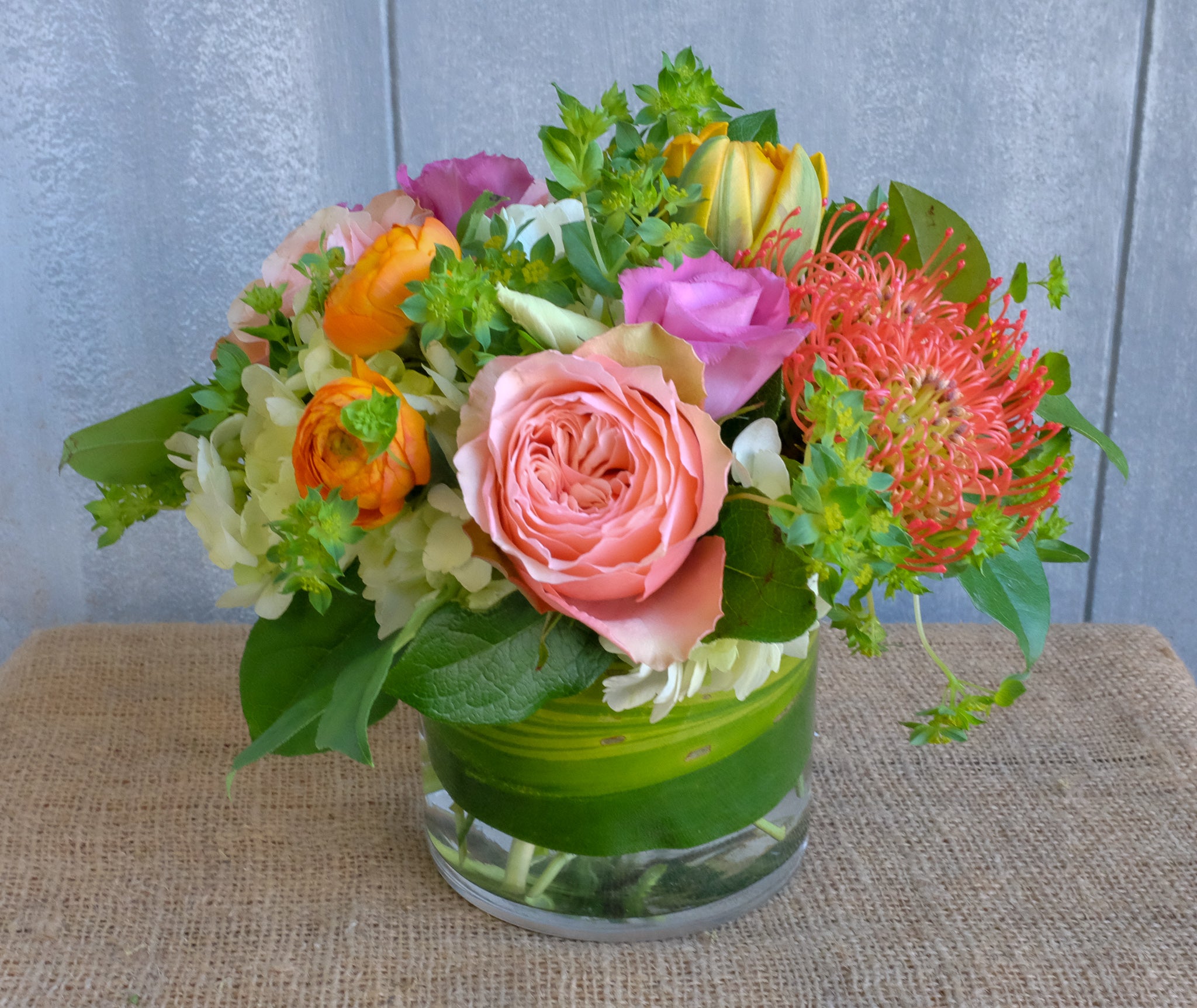 Low and lush centerpiece with Ranunculus, Double Orange Princess Tulips, and Protea | Michler's Florist