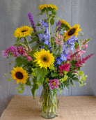 Tall and elegant summer bouquet featuring sunflowers, delphimium, and snapdragons designed by Michlers Florist in clear glass vase