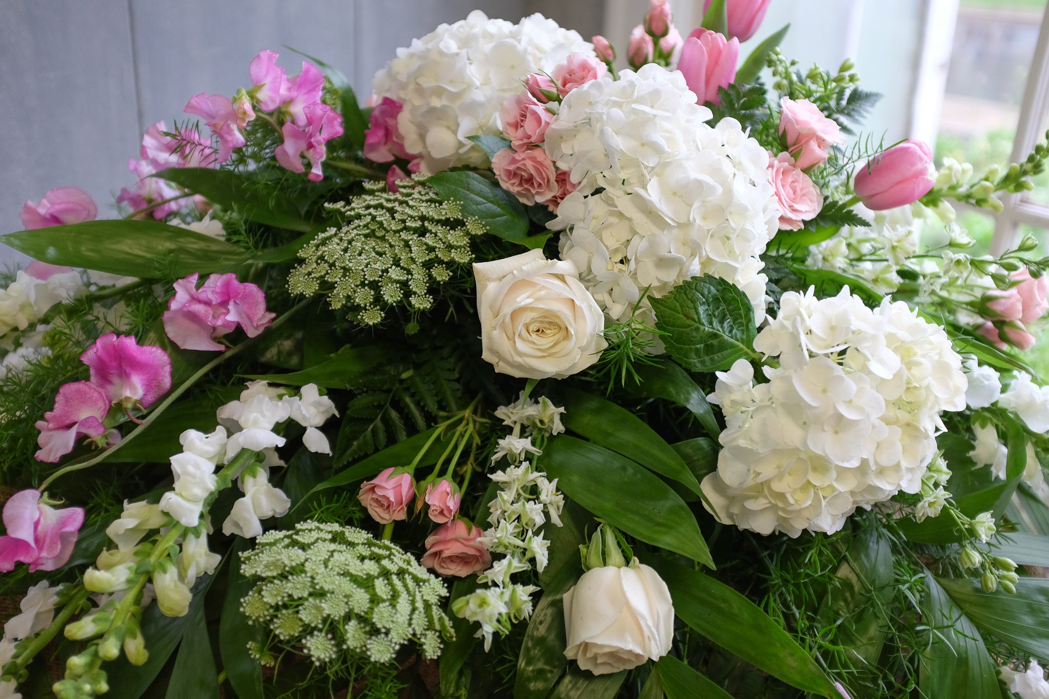 Close up image of floral details on a casket spray in pink and white with snapdragons, roses, hydrangea and tulips.
