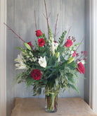 Tall bouquet of red and white Christmas flowers and evergreens in a glass vase, tall branches give this design a winter woodland feel