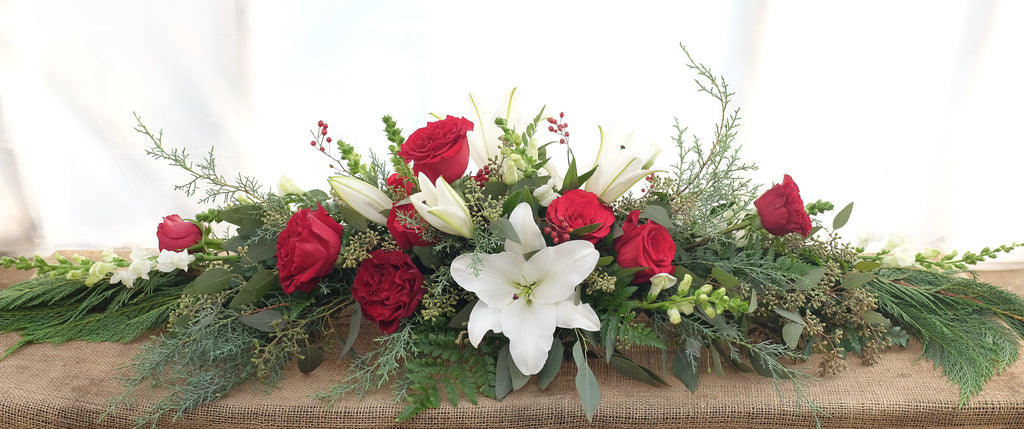 Low and long Christmas arrangement with white oriental lilies, red roses, and evregreens