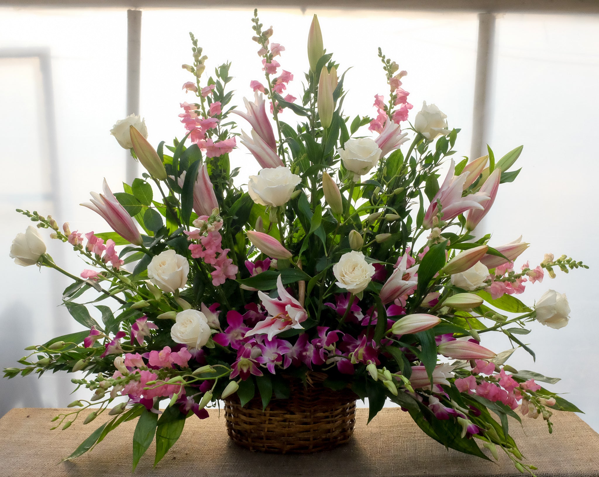 A funeral floral basket with stargazer lilies, pink snapdragon, white roses, dendrobium
