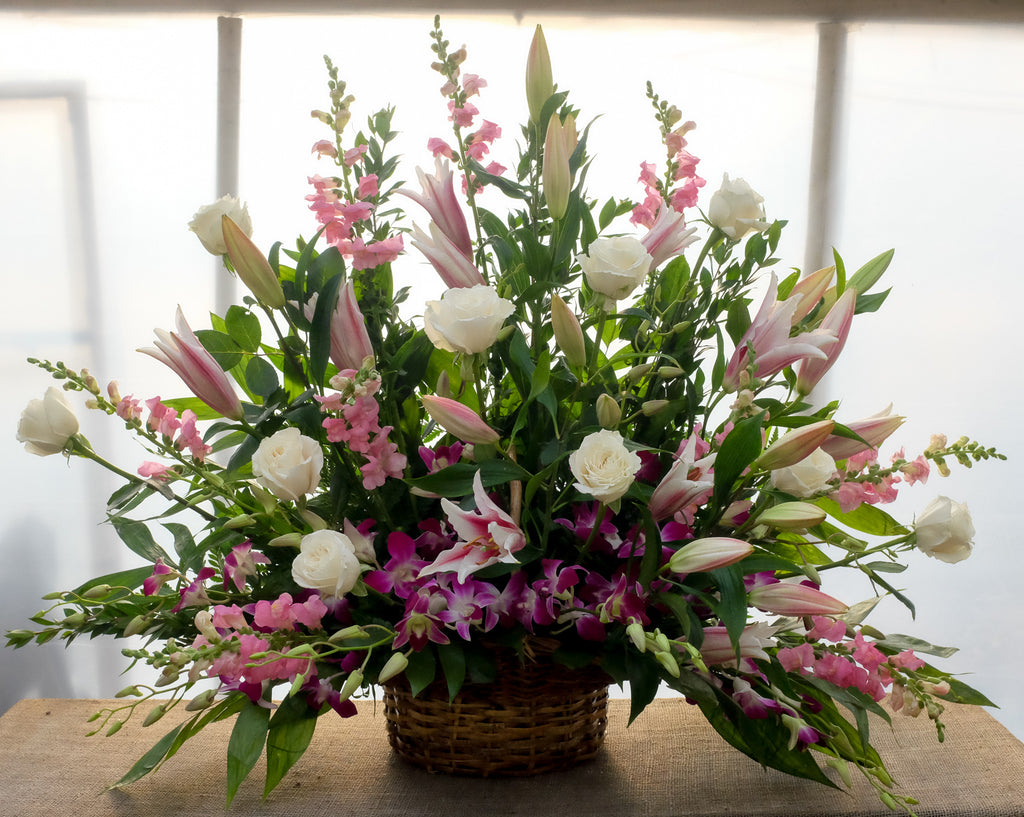 A funeral floral basket with stargazer lilies, pink snapdragon, white roses, dendrobium