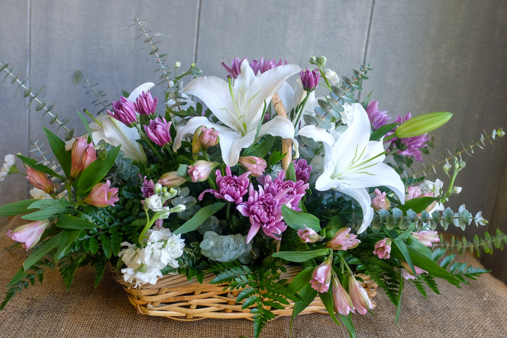 Arrangement in a basket with white lilies and purple and pink flowers