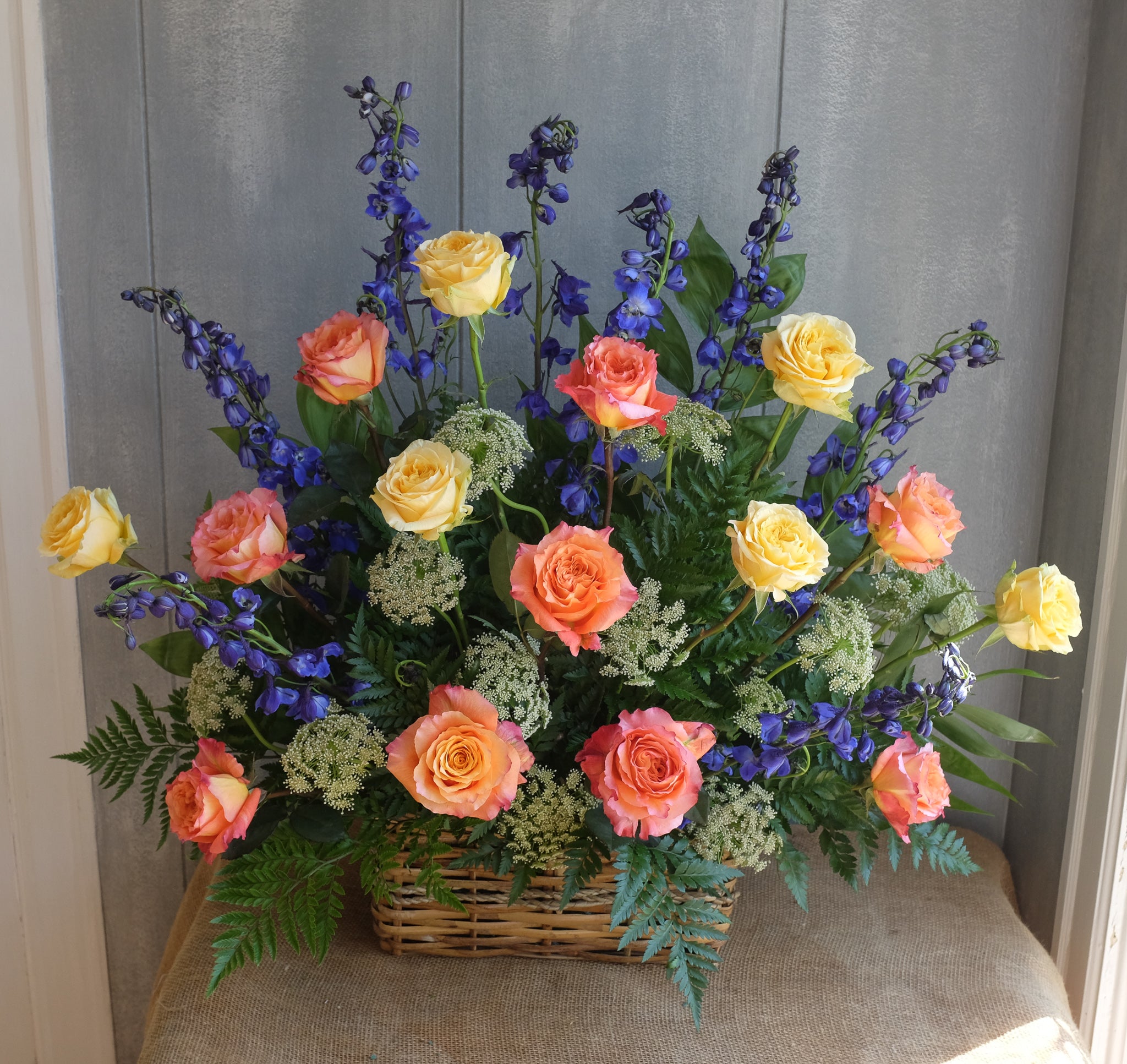 Flower basket with yellow and orange roses and blue delphinium