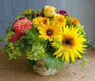 Lush bouquet filled with bright colors and summer flowers including sunflowers, zinnias, and green hydrangea designed by Michlers Florist in birch vase