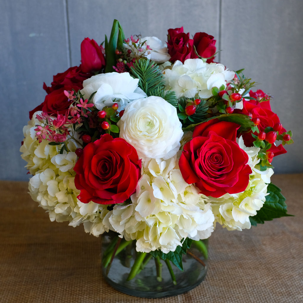 a low and lush flower arrangement with roses, hydrangea, ranunculus, and winter berries by Michler's