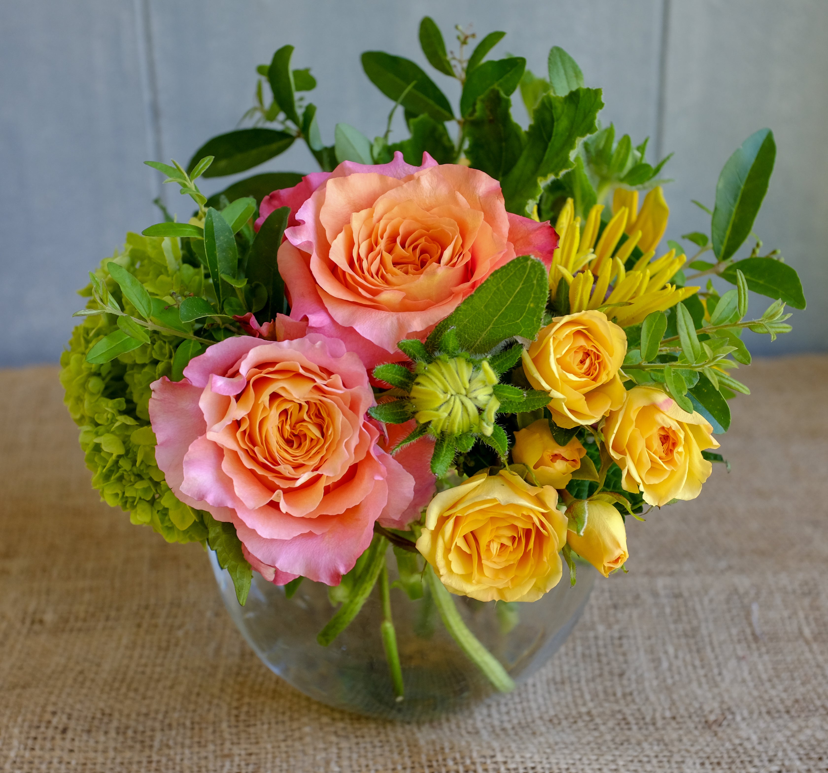 Cheerful low and lush bouquet with orange and yellow roses designed in bubble bowl