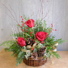 Basket of evergreens with red roses and woodland accents.