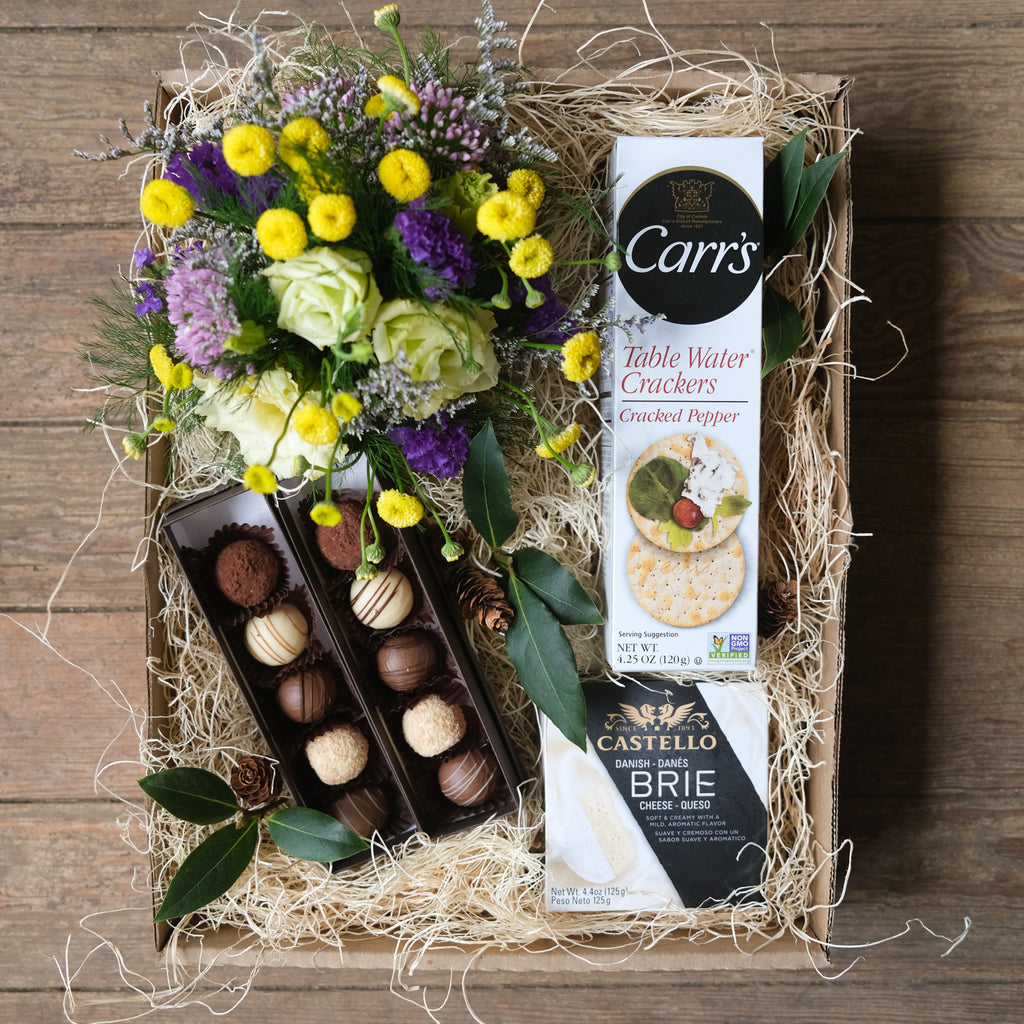 A box featuring a cheery flower arrangement, two boxes of chocolate truffles, crackers, and cheese.
